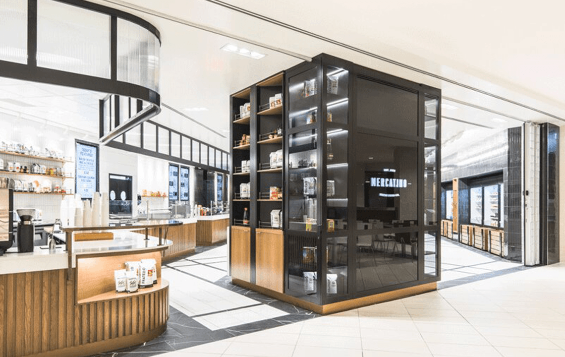 A big square shelving unit sits in the middle of a black and white tiled floor with a cafe bar to the left of it